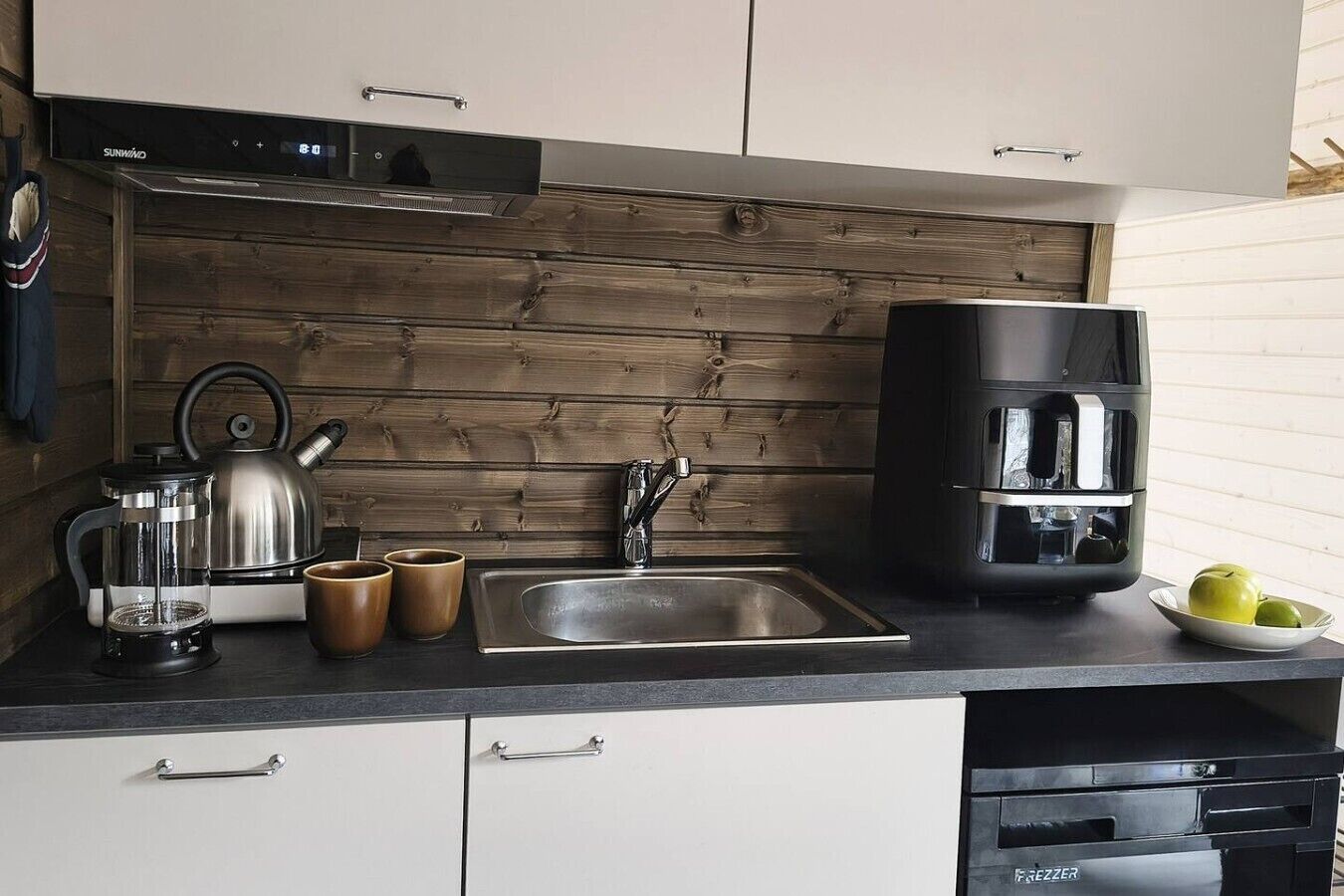 A modern kitchen with a stainless steel sink, a kettle, a coffee maker, and a dish rack.