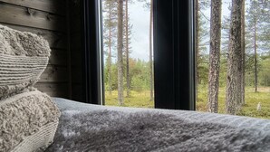 A bed with a grey blanket and a view of a forest through a window.