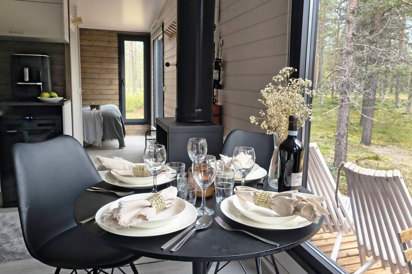 A dining table set for two with plates, glasses, and cutlery, a bottle of wine, and a vase with flowers.