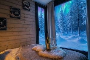 Una habitación acogedora con una pared de madera, una ventana con vistas a un bosque nevado y una mesa con una botella y vasos.