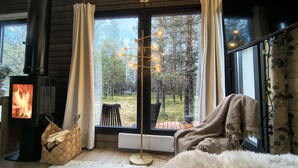 A cozy room with a wood-burning stove, a large window with curtains, a floor lamp, and a bench.
