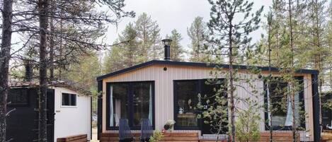 A cabin with a large window, a deck, and a chimney.