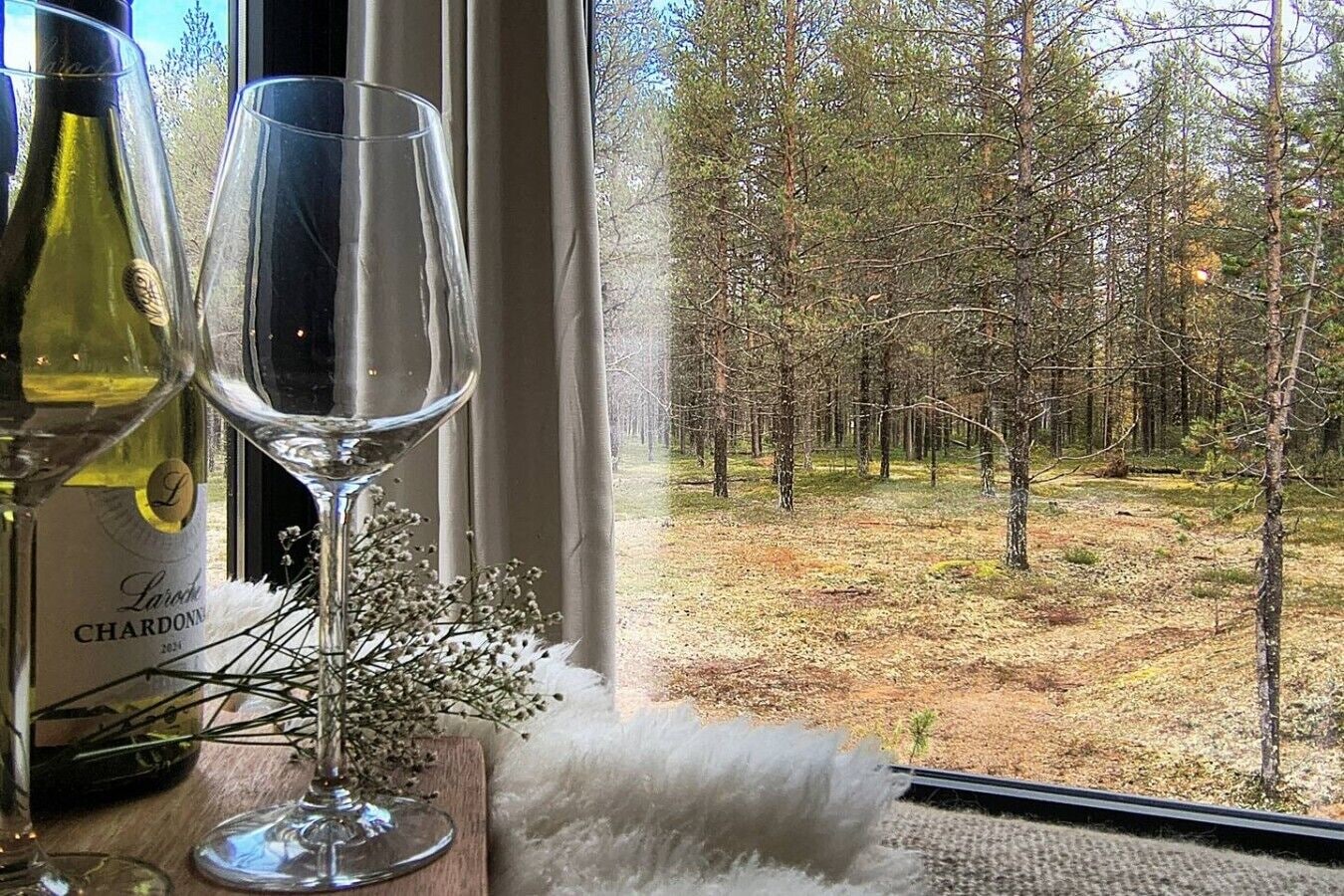 A window view of a forest with a bottle of wine and a glass on a windowsill.
