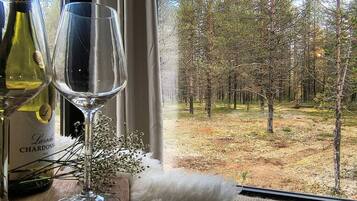 Vista desde la ventana: un bosque con una botella de vino y una copa en el alféizar.