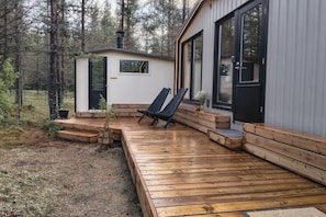 A wooden deck leading to a cabin with a small porch and two black chairs.