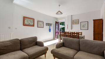 A living room with two sofas, a dining table with chairs, and a ceiling light fixture.