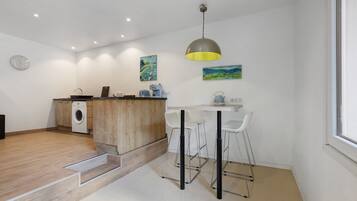 Cocina compacta con lavadora, encimera de madera y zona de comedor con taburetes de bar.