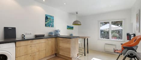 A modern kitchen with wooden cabinets, a built-in washing machine, and a dining area with a table and chairs.