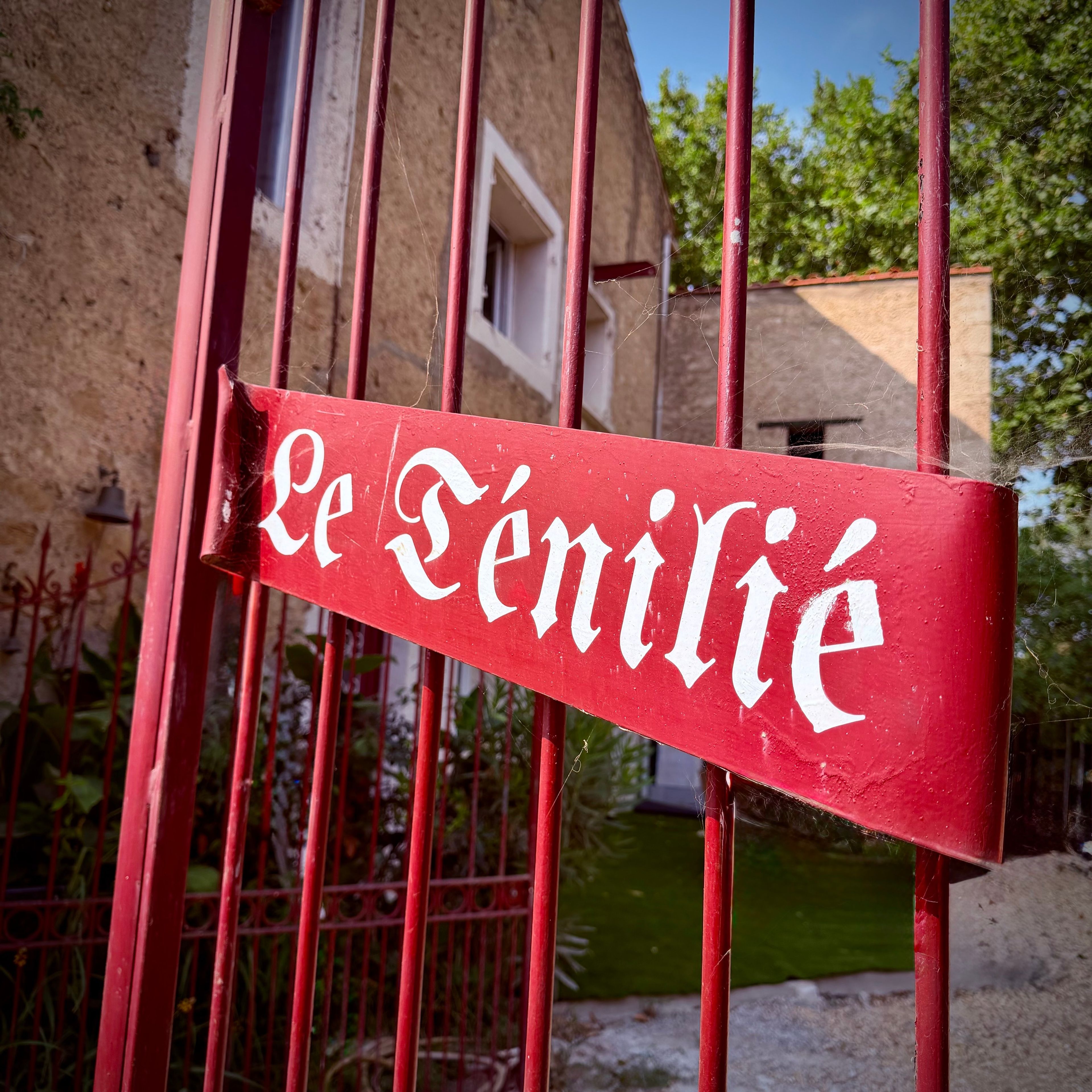 A red sign with white lettering on a metal gate, indicating the name 'Le Fenilie.'