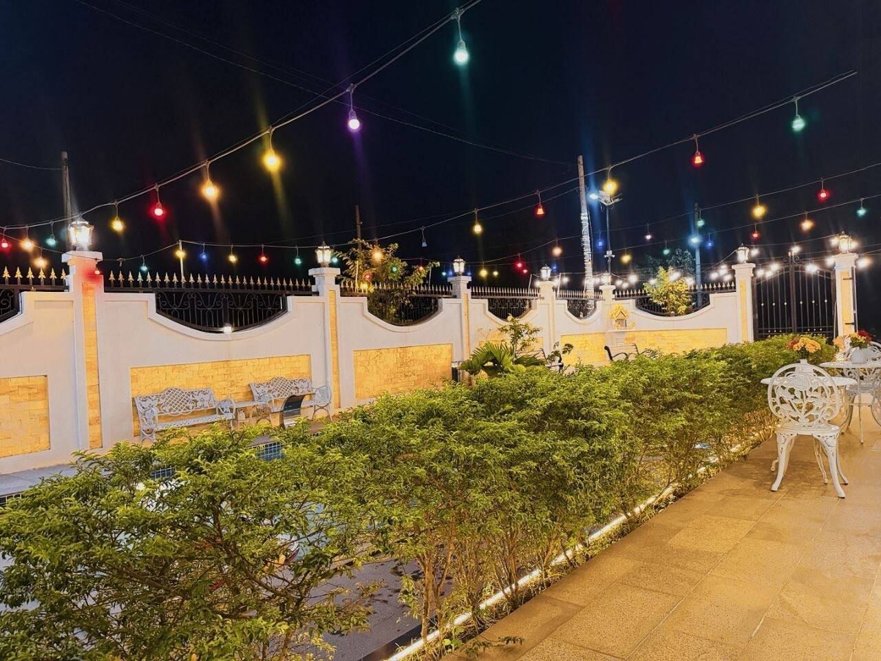 An outdoor area with a white fence, benches, and string lights.