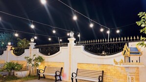 A well-lit outdoor area with two benches, a decorative fence, and a small ornamental structure.