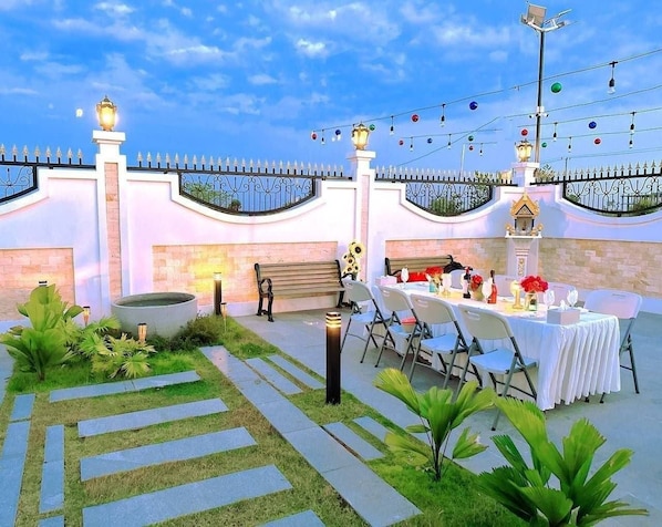 An outdoor dining area with a table set for a meal, surrounded by chairs and a decorative fence.