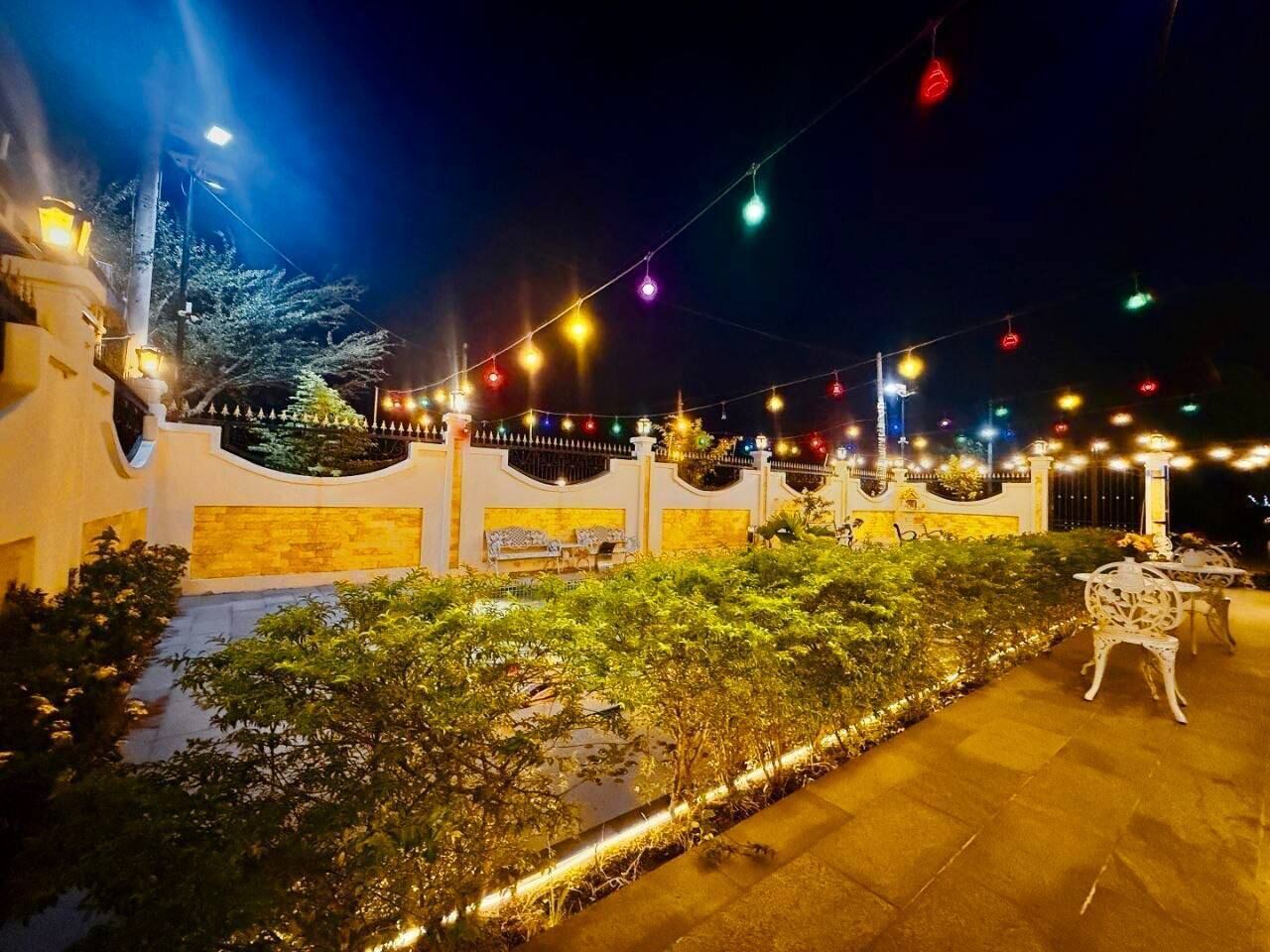 An outdoor area with a paved walkway, seating arrangements, and string lights.