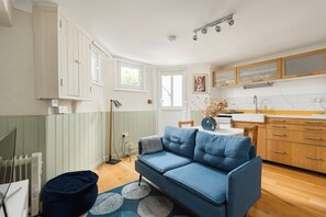 A modern kitchen with white cabinets, a blue sofa, and a dining table. - New! Cosy 1BR Flat w/Patio in New Cross (Greater London)
