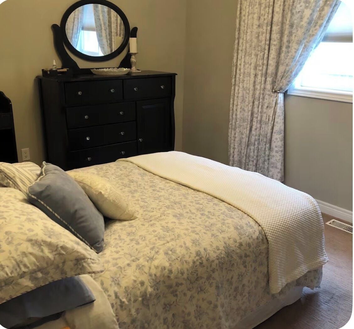Un dormitorio con una cama, un tocador con espejo y una ventana con cortinas.