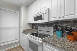 A kitchen with white cabinets, a microwave, an oven, and a granite countertop. - Fairway Serenity at River Club (Pawleys Island)