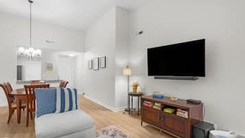 Ein Wohnzimmer mit Flachbildfernseher, einer Essecke mit Holzkohlen, einer Couch und einer kleinen Vitrine mit Büchern.