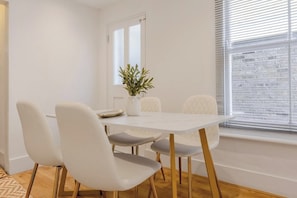 A dining area with a white table, four chairs, and a potted plant. - Trendy 3BR Fulham Home Near Chelsea w/Garden (Greater London)