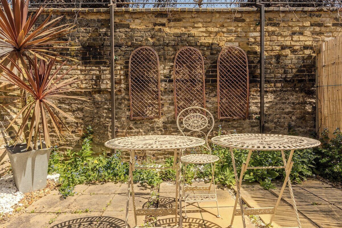 Een terras met metalen tafels en stoelen, een plant in pot en een stenen muur.