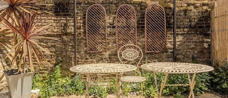A patio with metal tables and chairs, a potted plant, and a stone wall.