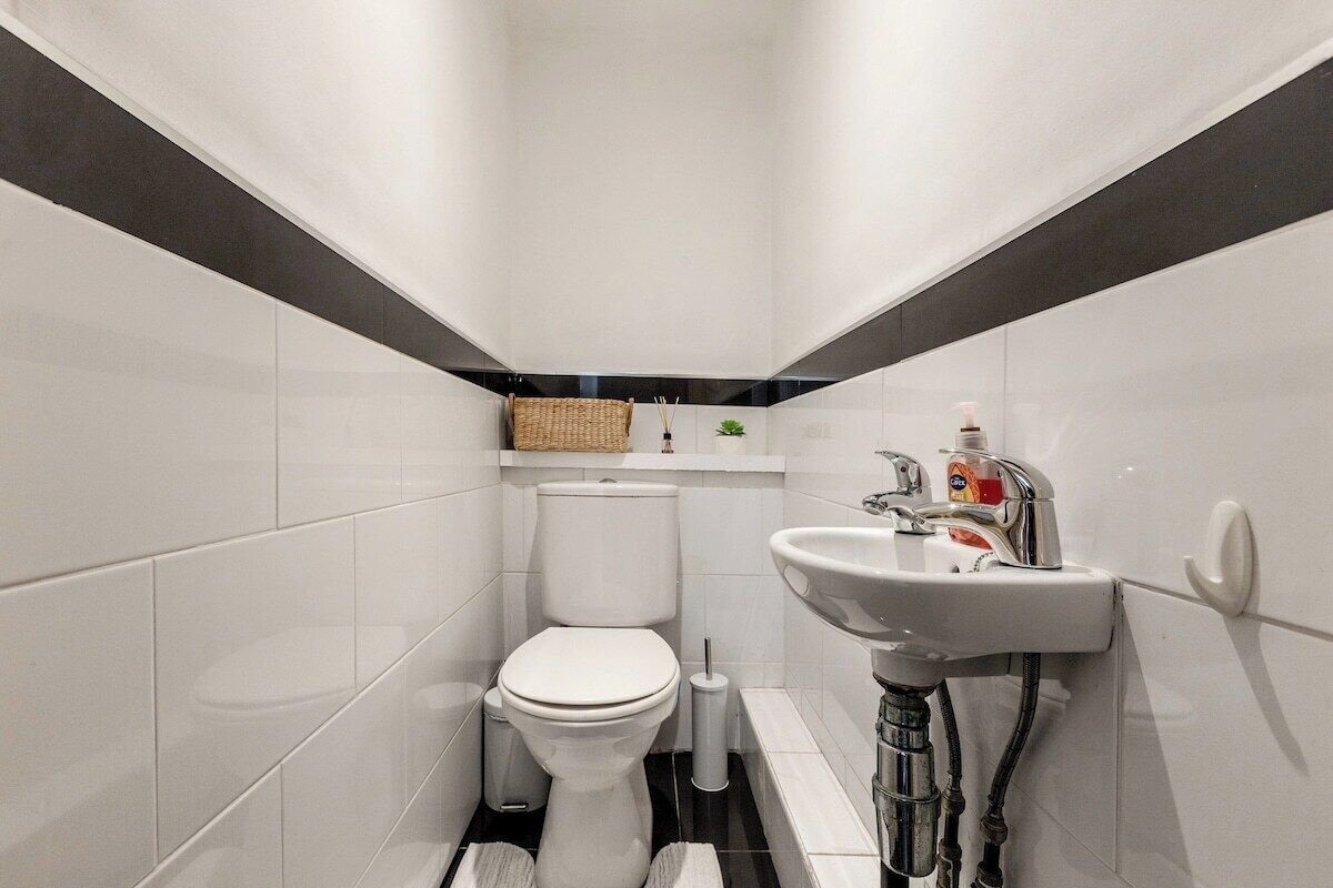 A small, modern bathroom with white tiles, a toilet, a sink, and a bidet.