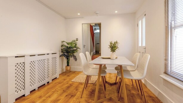 Et spiseområde med et hvidt bord og stole, en potteplante og en radiator.