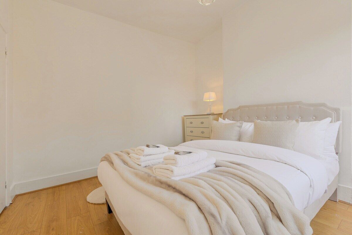 A neatly made bed with a fluffy white blanket, a bedside table with a lamp, and a nightstand with drawers.