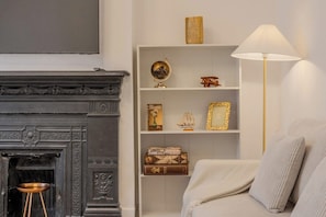 A room with a fireplace, a white bookshelf with decorative items, and a lamp. - Trendy 3BR Fulham Home Near Chelsea w/Garden (Greater London)