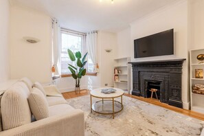 Ein Wohnzimmer mit einer Couch, einem runden Couchtisch, einem Kamin und einem an der Wand befestigten Fernseher.