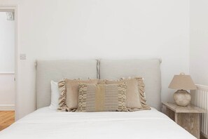 A bed with a headboard, two pillows, a bedside table with a lamp, and a wooden floor. - New! Wimbledon 4BR Home | Garden | 10 Mins to Tube (Greater London)