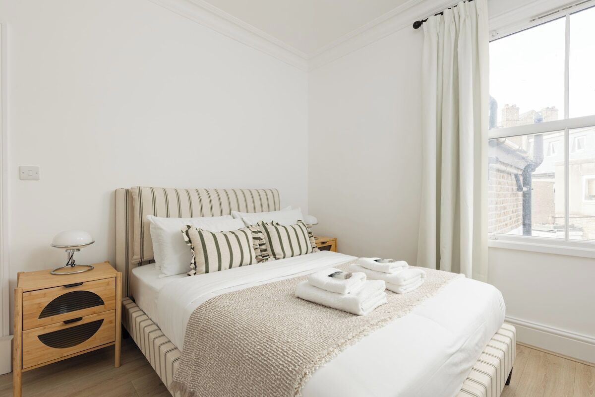 Ein ordentlich eingerichtetes Schlafzimmer mit einem Bett, einem Nachttisch und einem Fenster mit Vorhängen.