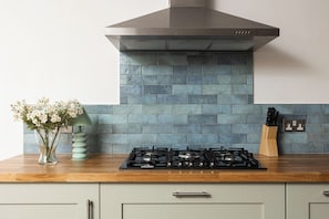 A kitchen with a gas stove, a stainless steel range hood, and a blue-tiled backsplash. - New! Wimbledon 4BR Home | Garden | 10 Mins to Tube (Greater London)
