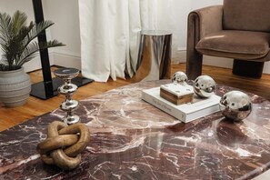 A living room with a marble coffee table, a potted plant, a modern chair, and a book titled 'The Art of Home'. - New! Wimbledon 4BR Home | Garden | 10 Mins to Tube (Greater London)