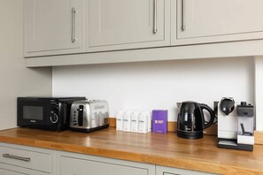 Une petite cuisine équipée d’un four à micro-ondes, d’un grille-pain, d’une machine à café et de distributeurs d’eau, le tout placé sur le plan de travail.