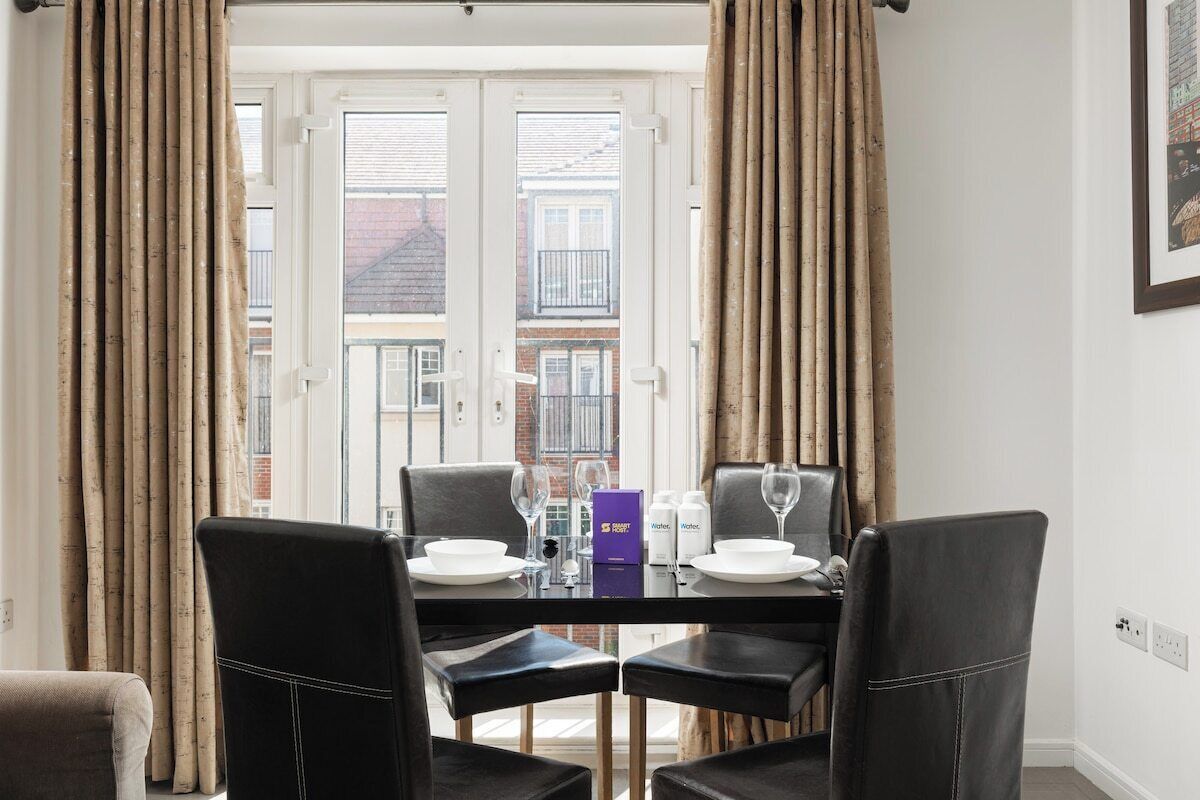 A dining area with a table set for two, two chairs, a glass, a bottle, and a box on the table.