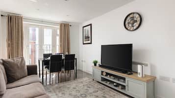 Un salon comprenant un canapé, un téléviseur à écran plat, un coin repas avec des chaises et un tapis à motifs.