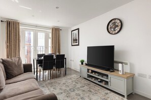 Ein Wohnzimmer mit Sofa, Flachbildfernseher, Essbereich mit Stühlen und einem gemusterten Teppich.