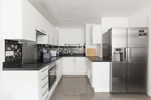 Eine moderne Küche mit weißen Schränken, einem Edelstahlkühlschrank und einer schwarzen Arbeitsplatte.