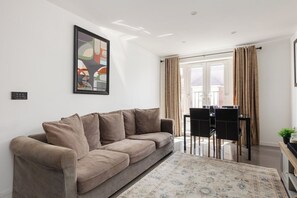 Ein Wohnzimmer mit einer Couch, einem Esstisch mit Stühlen, einem Teppich und einem Bild an der Wand.
