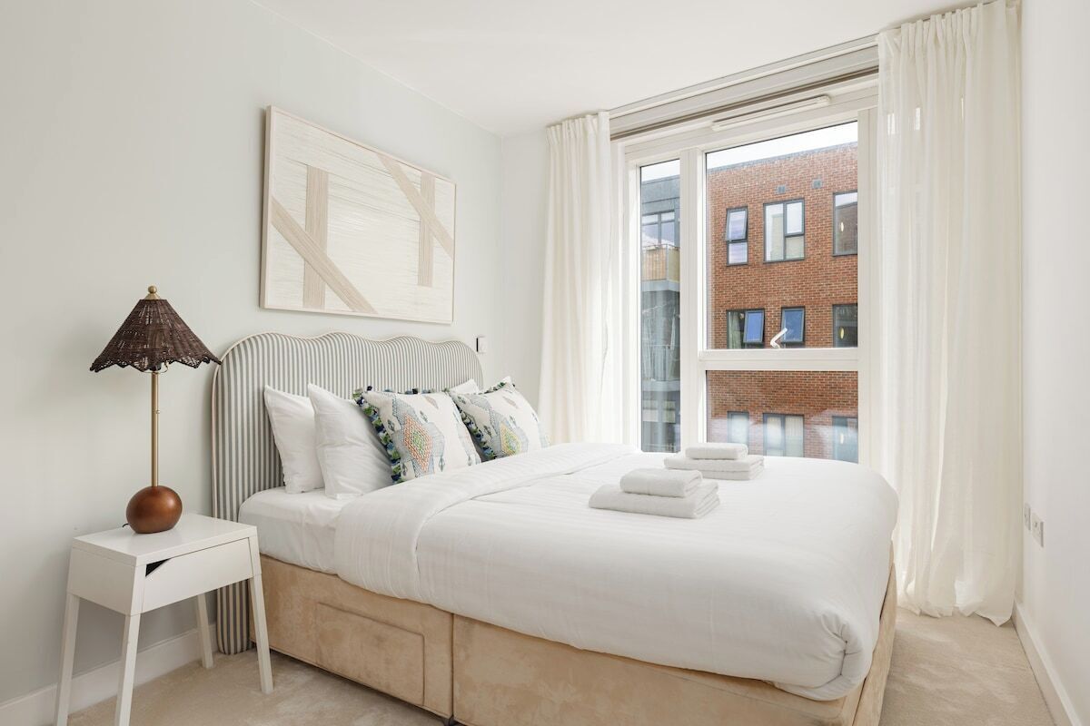 A bedroom with a bed, a bedside table, a lamp, and a window with curtains.