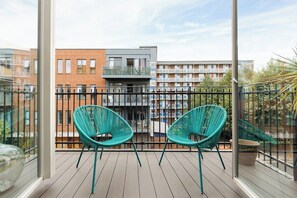 Ein Balkon mit zwei Stühlen, Blick auf ein mehrstöckiges Gebäude und einen klaren Himmel.