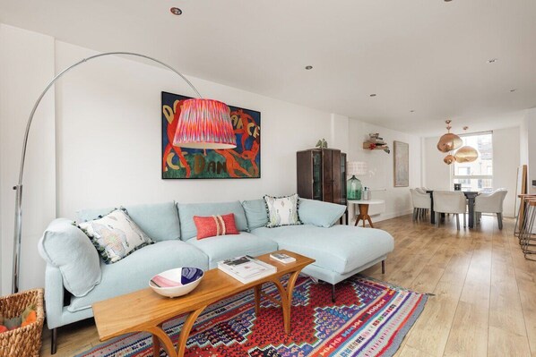 Ein modernes Wohnzimmer mit einem hellblauen Sofa, einem Holztisch und einem farbenfrohen Teppich.
