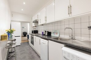 A modern kitchen with white cabinetry, a stainless steel sink, and a built-in dishwasher. - New! Charming 2BR Flat in Chelsea (Greater London)