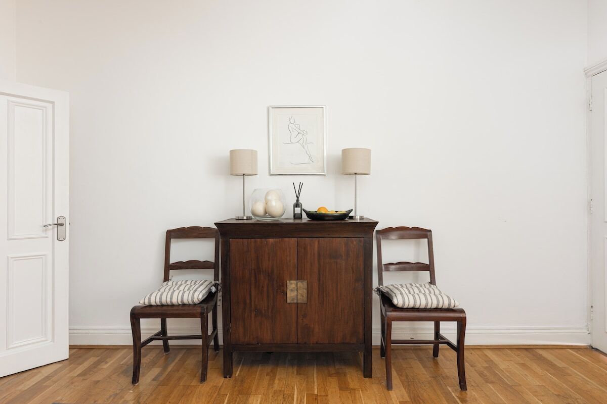A dining area with a wooden table and two chairs, a white door, and a framed artwork on the wall.