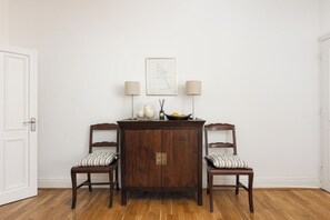 A dining area with a wooden table and two chairs, a white door, and a framed artwork on the wall. - New! Charming 2BR Flat in Chelsea (Greater London)