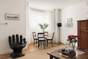 A modern living room with a dining area, a black sculptural chair, a vase with red flowers, and a table with an hourglass. - New! Charming 2BR Flat in Chelsea (Greater London)