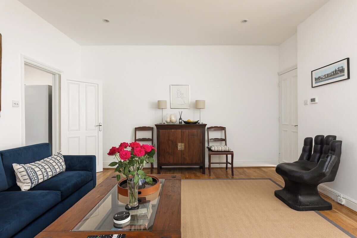 Una sala de estar con un sofá azul, una mesa de centro, un mueble de madera y una silla negra.
