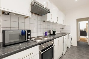 A modern kitchen with white cabinets, a built-in microwave, a stove, and a dishwasher. - New! Charming 2BR Flat in Chelsea (Greater London)