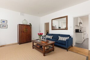 A living room with a blue sofa, a wooden coffee table, a cabinet, and a mirror on the wall. - New! Charming 2BR Flat in Chelsea (Greater London)