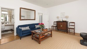 A living room with a blue sofa, a coffee table, a wooden cabinet, and a mirror on the wall. - New! Charming 2BR Flat in Chelsea (Greater London)